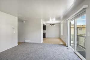Living room with light carpet, a chandelier in dining room, and sliding glass door to balcony