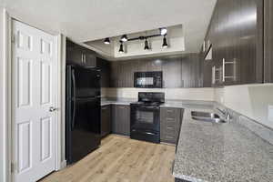 Kitchen featuring a textured ceiling, black appliances, light stone counters, light wood-style floors.