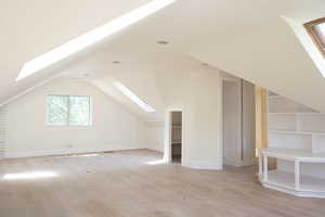Additional living space with a skylight, light wood finished floors, and vaulted ceiling
