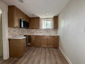 Kitchen with tasteful backsplash, brown cabinetry, dark wood-type flooring, light countertops, and black microwave
