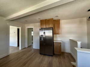 Kitchen with brown cabinets, stainless steel fridge, a textured ceiling, dark wood finished floors, and light countertops