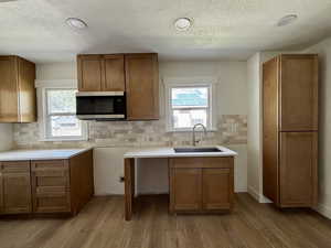 Kitchen featuring brown cabinetry, a textured ceiling, stainless steel microwave, and dark wood-style flooring