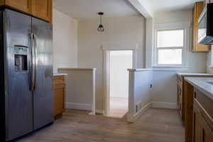 Kitchen with brown cabinetry, stainless steel appliances, pendant lighting, dark wood-type flooring, and light countertops