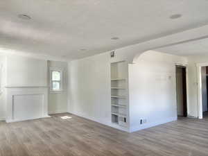 Unfurnished room with a textured ceiling, light wood-type flooring, built in shelves, and arched walkways