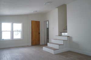 Foyer entrance featuring light wood-type flooring, vaulted ceiling, stairway, and a textured ceiling