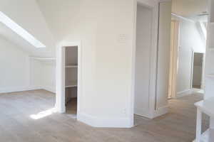 Additional living space featuring a skylight, light wood finished floors, and lofted ceiling