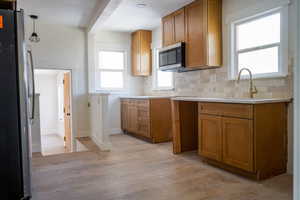 Kitchen featuring appliances with stainless steel finishes, brown cabinets, light wood-type flooring, light countertops, and tasteful backsplash
