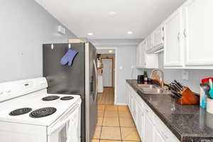 Kitchen featuring white electric range oven, tile counters, white cabinets, light tile patterned floors, and recessed lighting