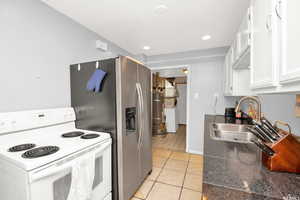 Kitchen featuring white electric stove, white cabinetry, strapped water heater, light tile patterned floors, and washer / dryer