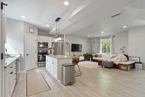 Kitchen with decorative light fixtures, a kitchen breakfast bar, white cabinets, a center island, and stainless steel appliances