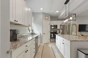 Kitchen with white cabinets, light stone countertops, stainless steel appliances, light wood-style flooring, and recessed lighting