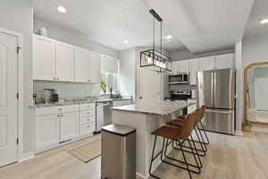 Kitchen featuring light stone counters, stainless steel appliances, a kitchen bar, a center island, and white cabinets
