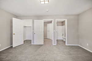 Unfurnished bedroom with a walk in closet, light colored carpet, ensuite bathroom, and a textured ceiling