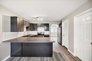 Kitchen featuring arched walkways, decorative backsplash, appliances with stainless steel finishes, a peninsula, and light wood-type flooring
