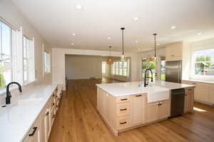 Kitchen featuring light LVP floors, stainless steel appliances, recessed lighting, a kitchen island with sink, and decorative light fixtures