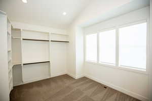 Master walk in closet with carpet floors and vaulted ceiling