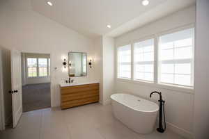 Master bath with two vanities, a soaking tub, vaulted ceiling, tile patterned flooring, and a tiled oversize shower