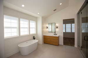 Master bath with two vanities, a soaking tub, vaulted ceiling, tile patterned flooring, and a tiled oversize shower