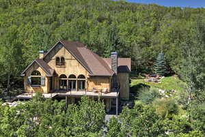 Rear view of house featuring a chimney, a forest view, a shingled roof, a deck, and stone siding