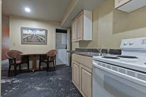 Kitchen with electric stove, stacked washer / dryer, dark countertops, concrete floors, and light brown cabinets