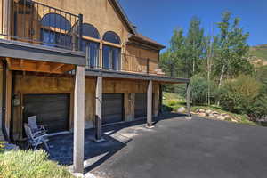 View of side of property featuring a balcony, an attached garage, driveway, and a patio area