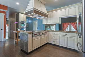 Kitchen with a peninsula, dark wood-style floors, stainless steel appliances, premium range hood, and recessed lighting