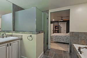 Ensuite bathroom with vanity, a garden tub, tiled shower, ceiling fan, and a textured ceiling