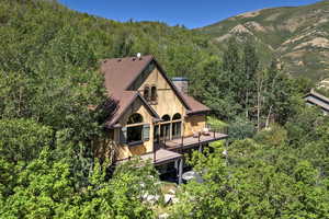Back of house featuring a deck with mountain view, a chimney, a view of trees, and a shingled roof