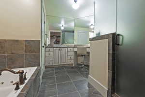 Bathroom featuring a tub with jets, vanity, and tile walls