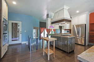 Kitchen featuring dark wood-style floors, stainless steel appliances, a peninsula, custom exhaust hood, and a textured ceiling