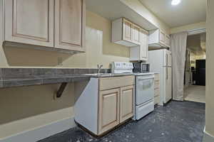 Kitchen with white range with electric stovetop, concrete floors, light brown cabinets, and stainless steel microwave