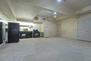 Kitchen featuring black appliances, light carpet, and a textured ceiling