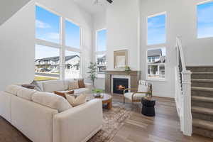 Living area with a high ceiling, stairs, wood finished floors, a lit fireplace, and ceiling fan