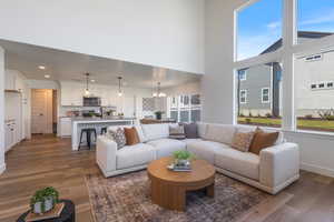 Living room with a chandelier, dark wood-style floors, a towering ceiling, and recessed lighting