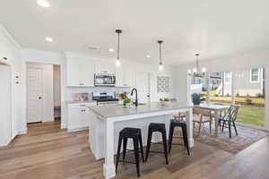 Kitchen with white cabinetry, hanging light fixtures, stainless steel appliances, tasteful backsplash, and recessed lighting