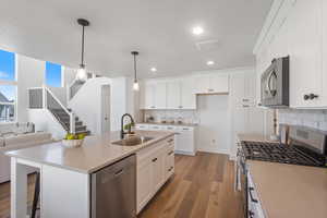 Kitchen featuring appliances with stainless steel finishes, open floor plan, light wood-style flooring, white cabinets, and a kitchen island with sink