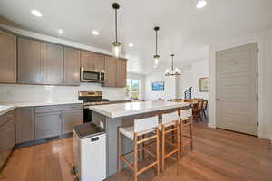 Kitchen featuring light wood-type flooring, a kitchen island, stainless steel appliances, a kitchen bar, and recessed lighting