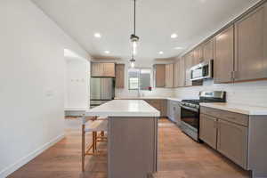 Kitchen featuring stainless steel appliances, backsplash, pendant lighting, a kitchen island, and a kitchen breakfast bar