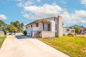 Raised rambler/ranch style home with a porch, a chimney, stairway, and driveway