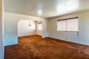 Unfurnished room featuring arched walkways, dark colored carpet, and a chandelier