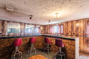 Indoor dry bar featuring wood paneling walls and a textured ceiling