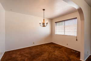 Empty room featuring dark carpet, a chandelier, and arched walkways