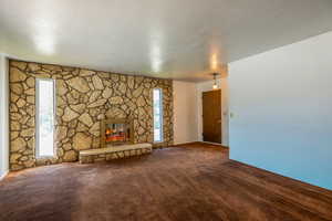 Unfurnished living room featuring dark carpet and a wood burning stone fireplace