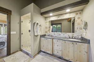 Ensuite bathroom with double vanity, a stall shower, tasteful backsplash, and beam ceiling