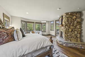Bedroom featuring hardwood / wood-style flooring, access to outside, a stone fireplace, and recessed lighting