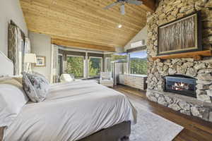 Bedroom with wooden ceiling, a stone fireplace, wood finished floors, high vaulted ceiling, and an AC wall unit