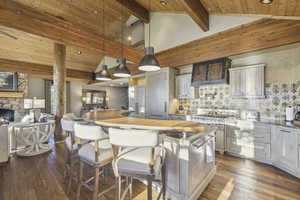 Kitchen with decorative light fixtures, decorative backsplash, high vaulted ceiling, a kitchen bar, and dark wood-type flooring