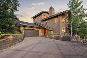 View of front of home featuring stone siding, concrete driveway, a garage, and a chimney