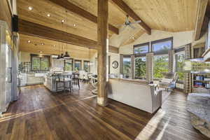 Living area featuring high vaulted ceiling, dark wood-style floors, plenty of natural light, a wood ceiling with exposed beams, and a ceiling fan