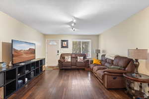 Living room with dark wood-style floors, track lighting, and a textured ceiling